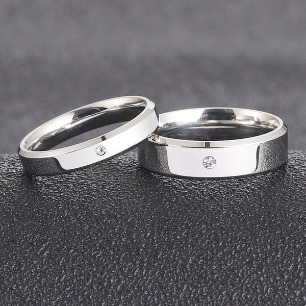 A simple, single-stone, silver-colored couple's ring