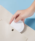 Hand placing white travel charging cable storage solution into beige purse pocket for easy portability